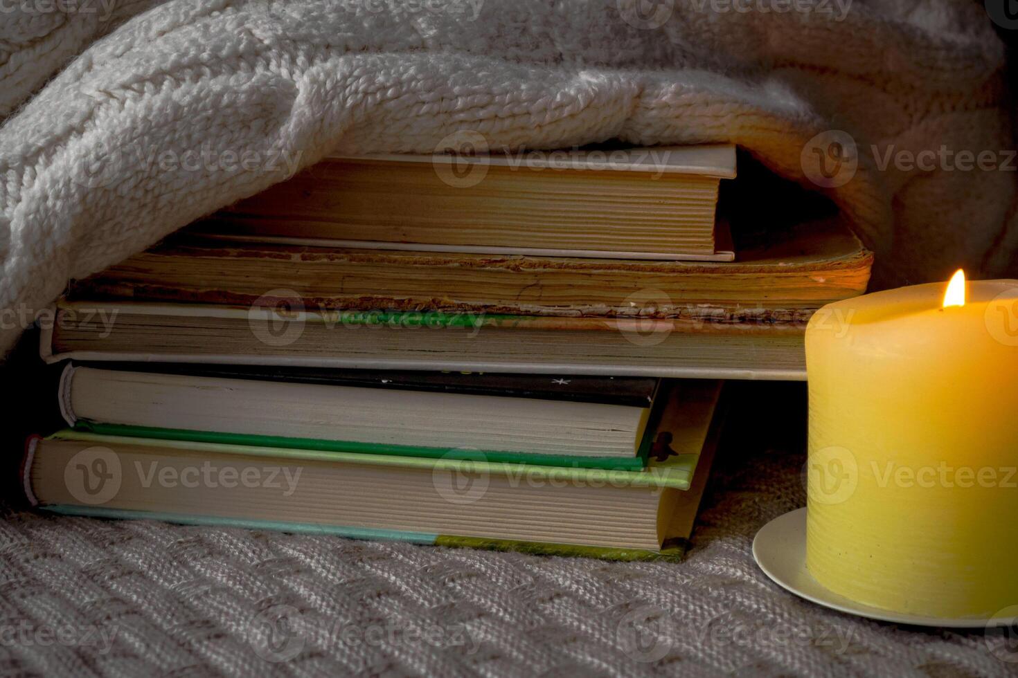 A stack of books and a warm sweater on a knitted plaid by candlelight photo