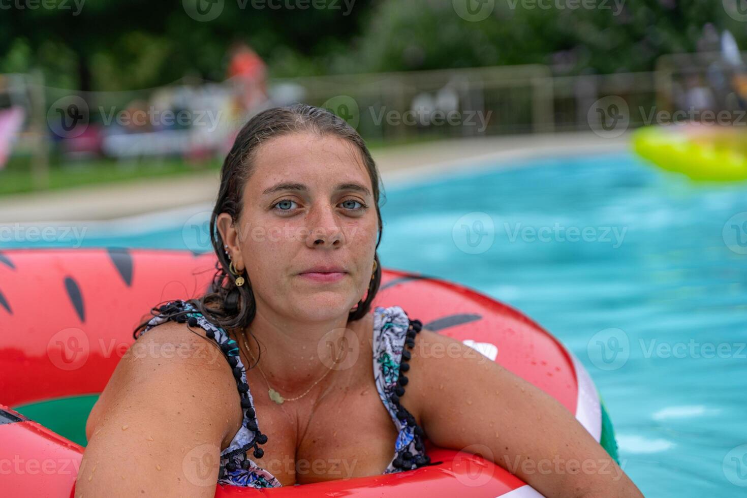 portrait of young woman in swimsuit inside big red lifebuoy in swimming pool during summer vacation photo