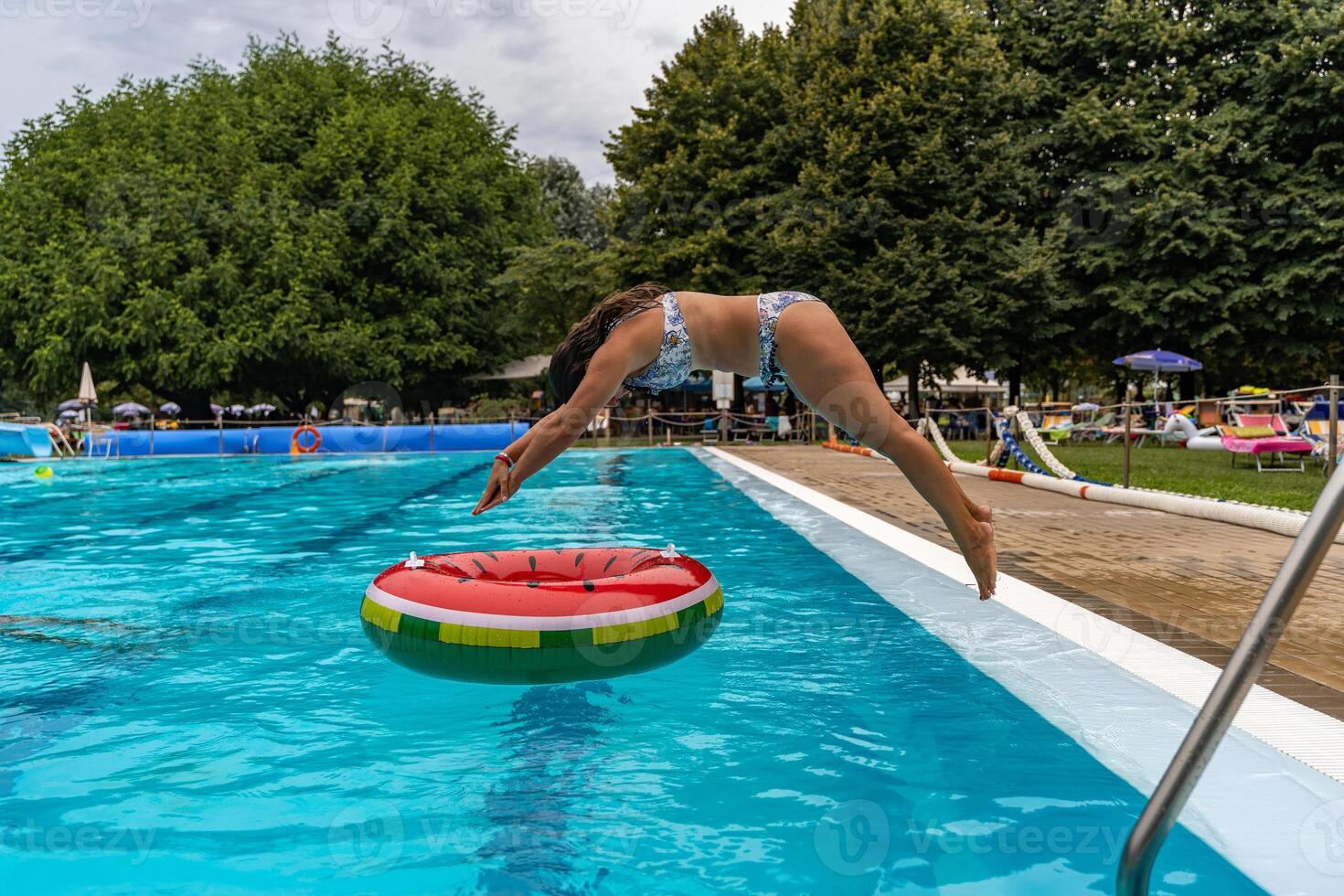young woman in swimsuit playfully diving from the edge of a swimming pool into a round lifebuoy photo