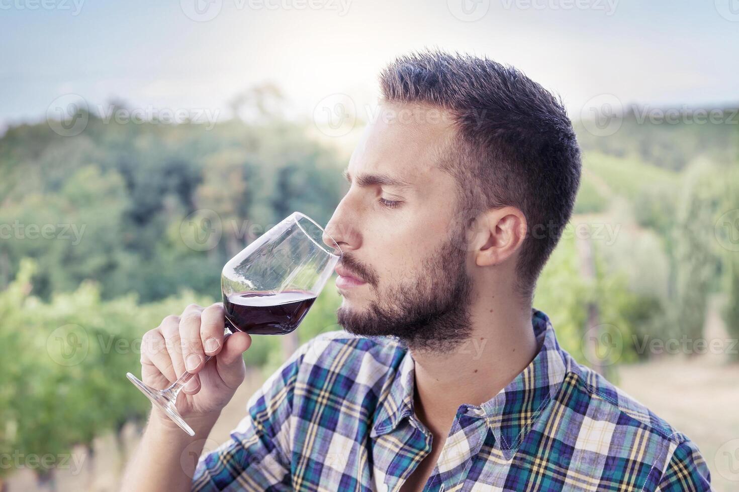 handsome bearded man sniffs glass of wine before drinking photo