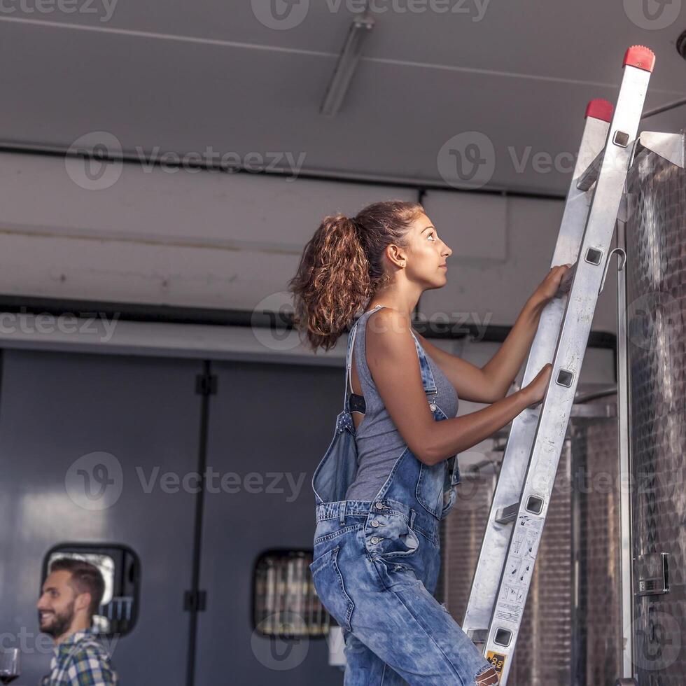 female winemaker controls the quality of wine on ladder over tank photo