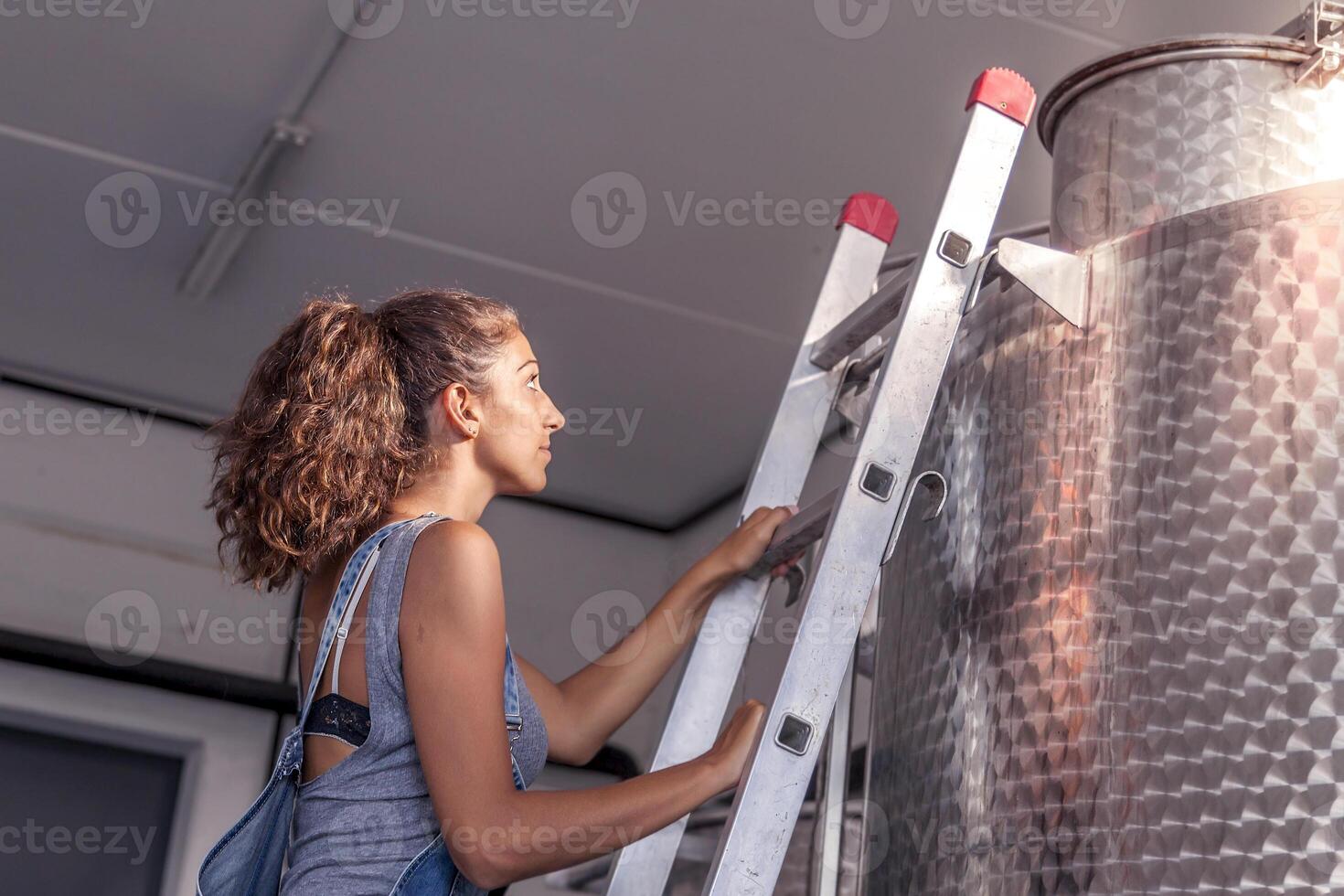 female winemaker controls the quality of wine on ladder over tank photo
