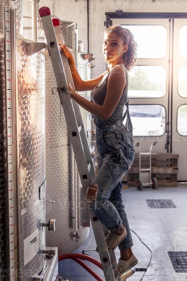 female winemaker controls the quality of wine on ladder over tank photo