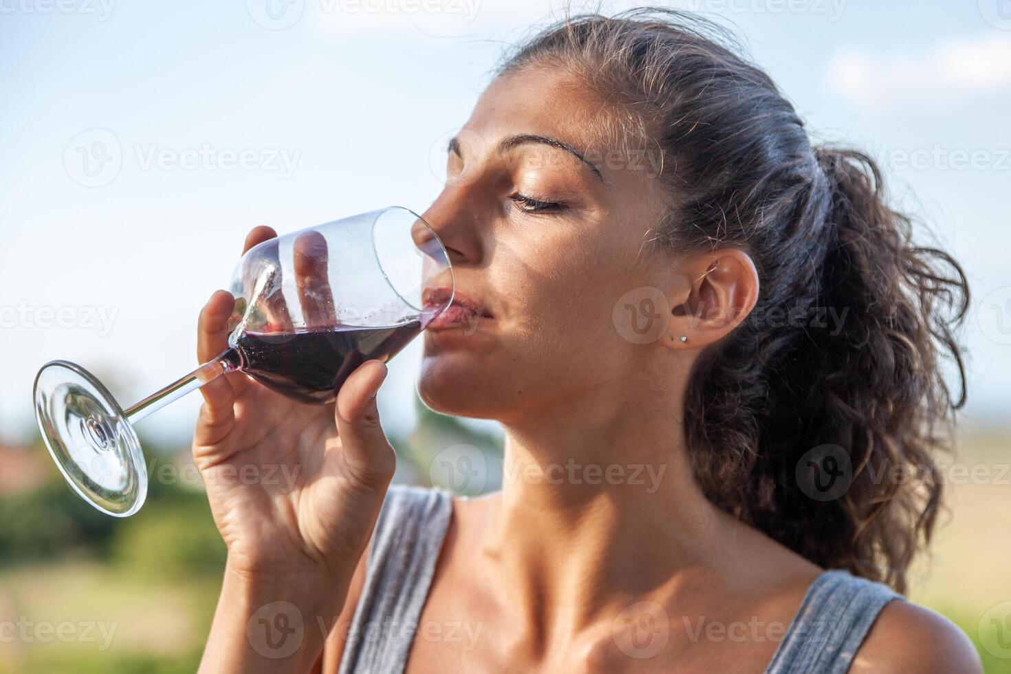 cute young adult woman tasting red wine from a glass tumbler photo