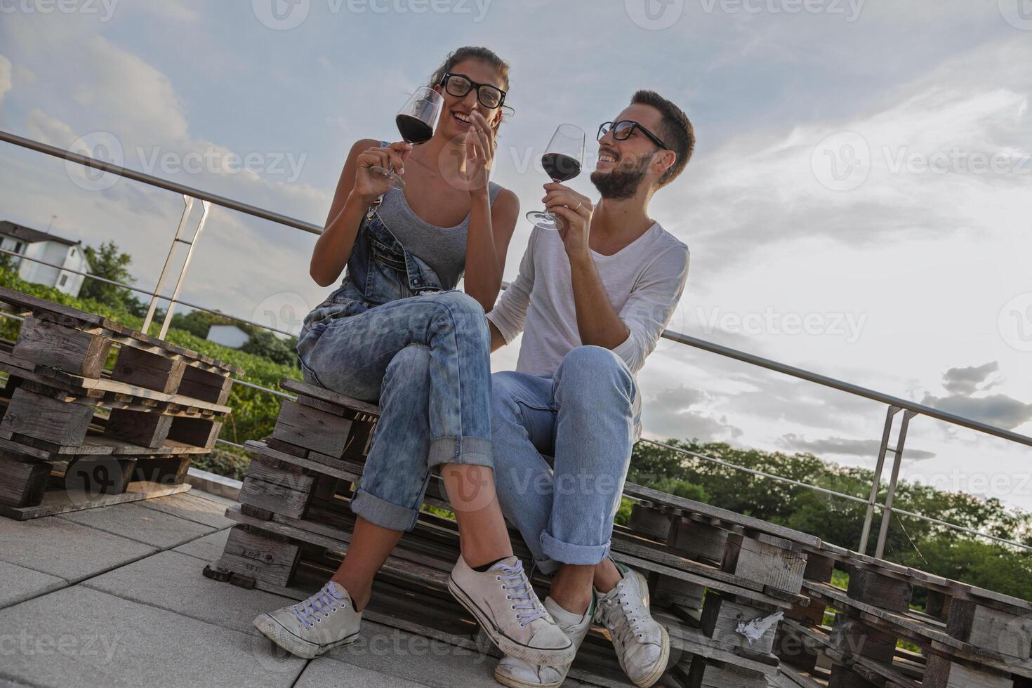 young couple of winemakers tasting red wine from a glass sitting outdoors surrounded by vineyards in autumn photo