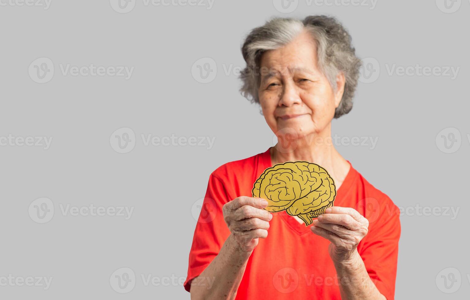 Portrait of a senior woman holding a brain shape made from yellow paper against a gray background photo