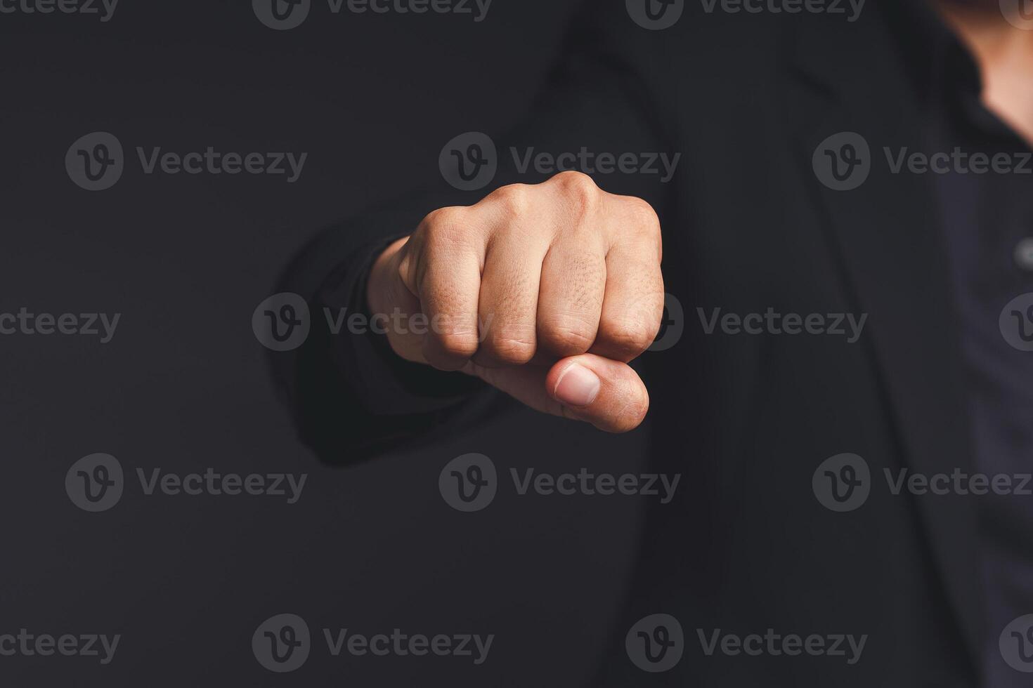 A businessman in a black suit raises his fist to the front, showing determination, and encouragement while standing on a black background photo