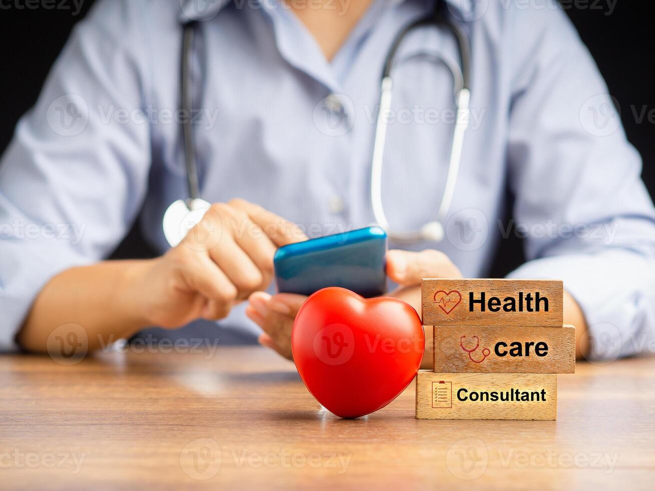 A doctor uses a smartphone and wooden cubes with icons of health and a red heart shape over the wooden desk while sitting in the hospital photo
