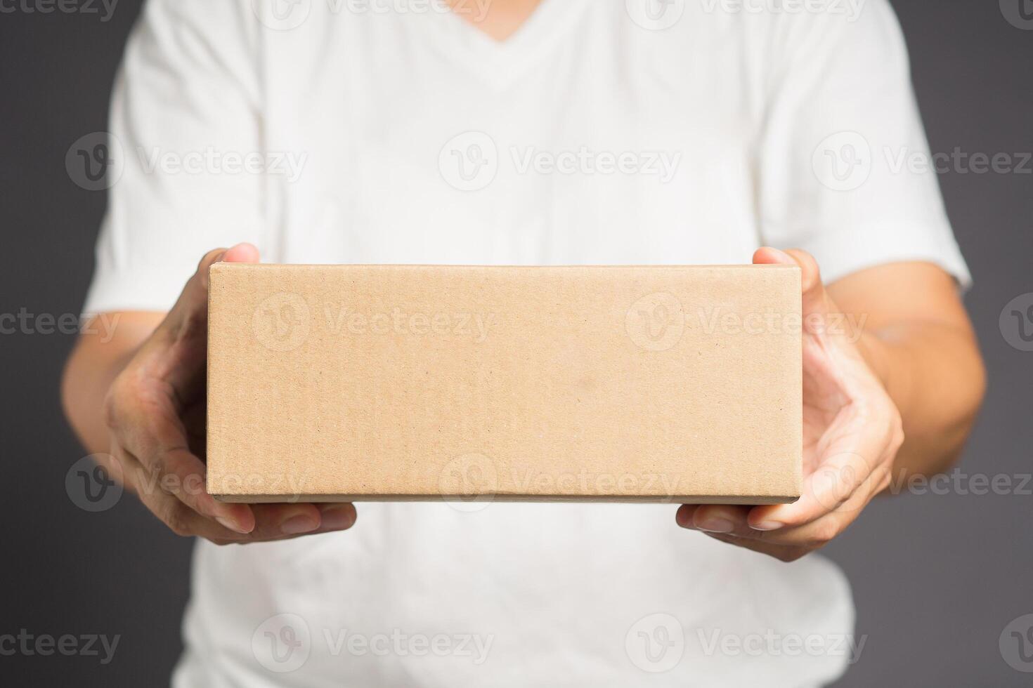 Man in white casual holding a cardboard box while standing on a gray background photo