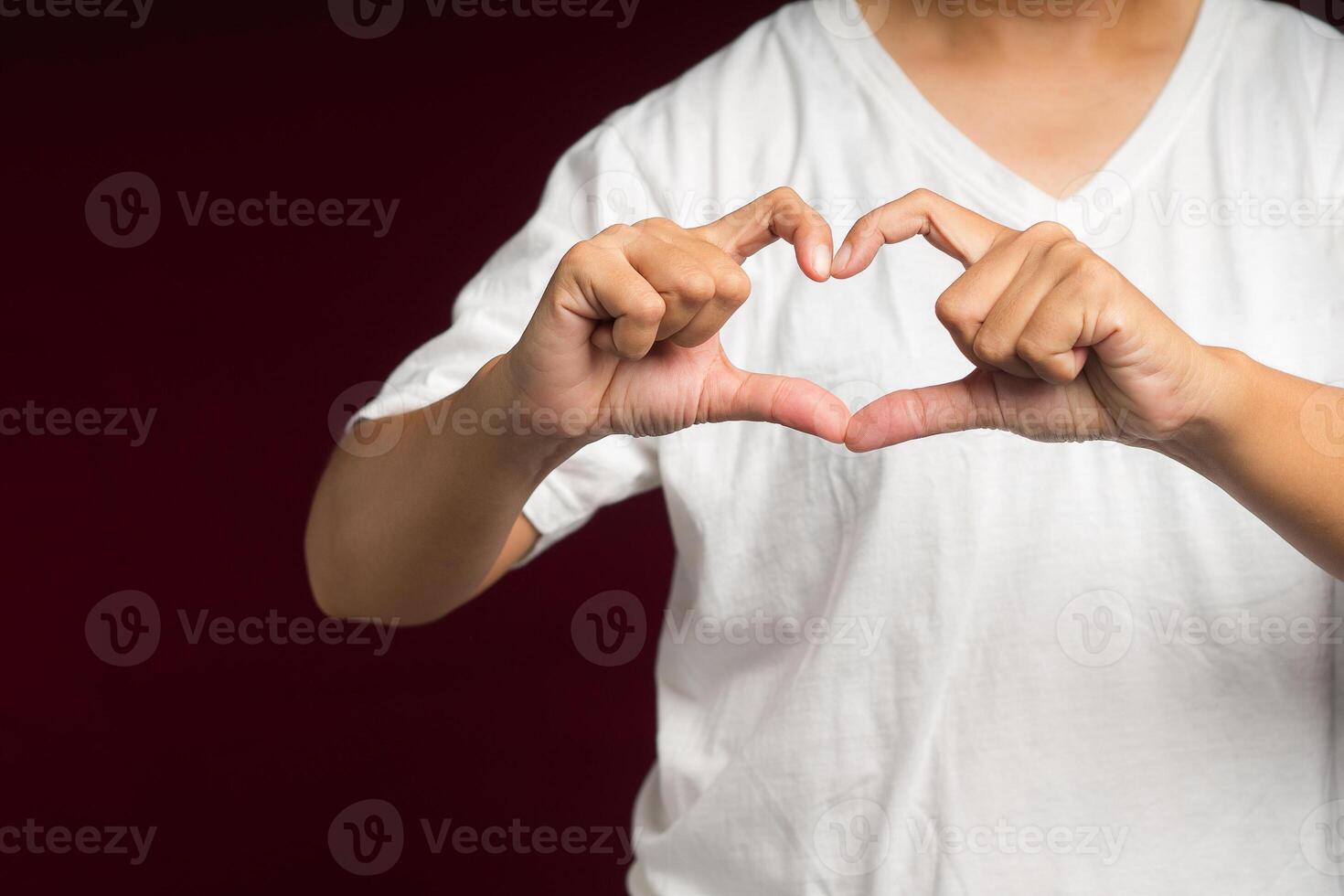 Man in white casual making heart figure love sign with fingers while standing on a red background photo