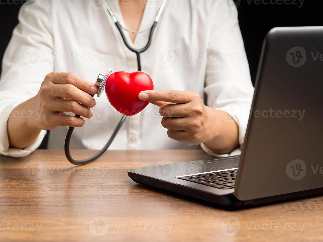 A doctor hand holding a stethoscope checking a red heart shape while sitting in the hospital or clinic photo