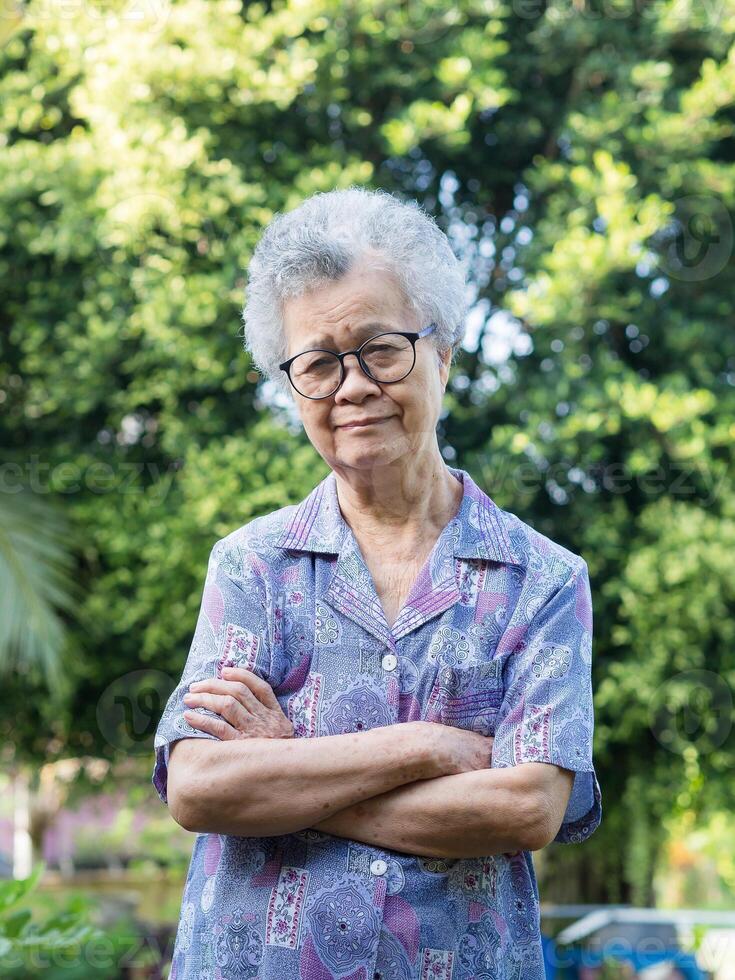 Portrait of a senior woman with short gray hair looking at the camera with a smile while standing arms crossed in the garden photo