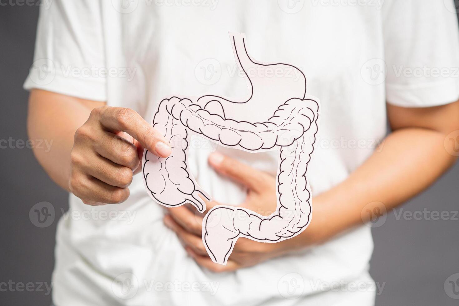 Hand holding a colon shape symbol and touching the stomach while standing on a gray background photo
