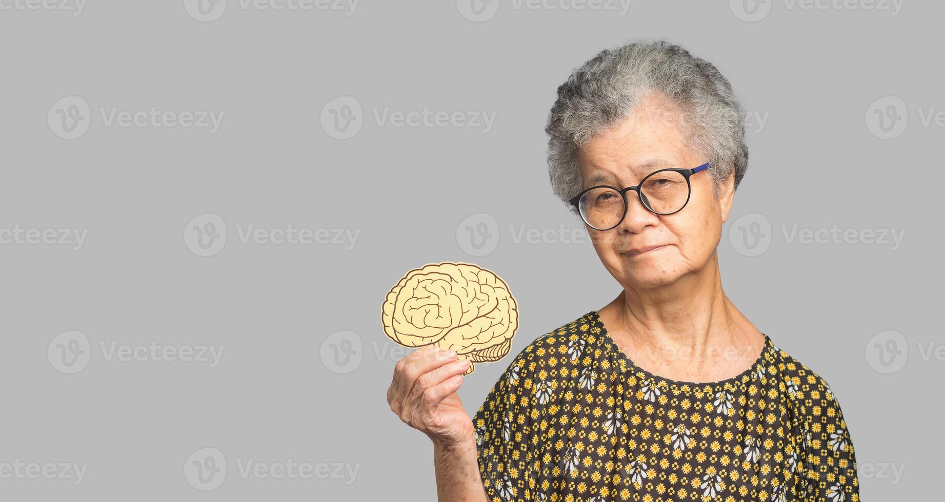 Portrait of a senior woman holding a brain symbol while standing on a gray background photo