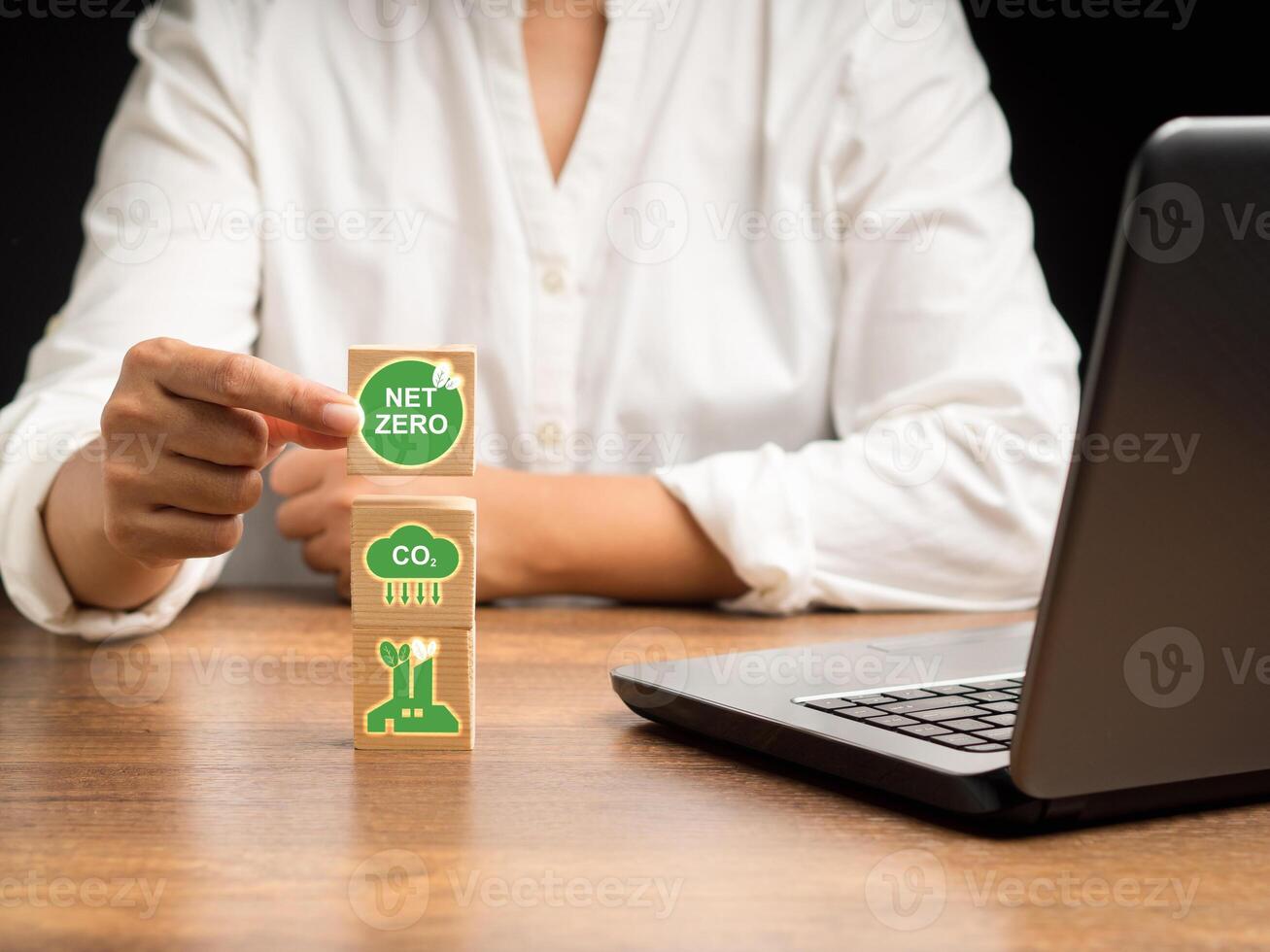 Net-zero greenhouse gas emissions target. Hand holding a wooden cube with green icons over a wooden table while sitting in the offic photo
