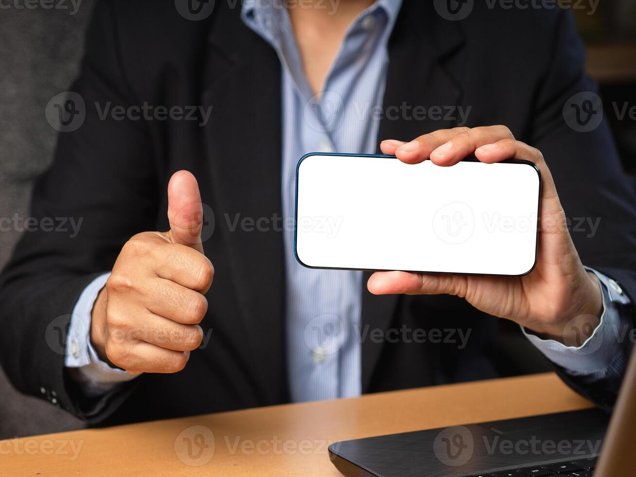 Hand holding a horizontal mobile phone with a blank white screen and showing thumbs up while sitting in the office photo