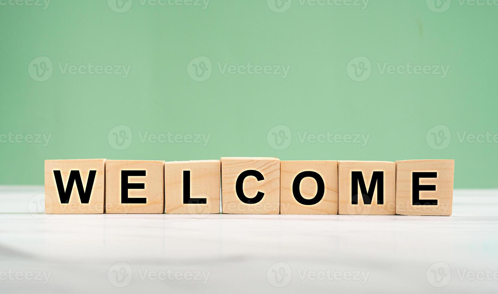 Welcome word is written on wooden cubes on a marble floor with a green background photo