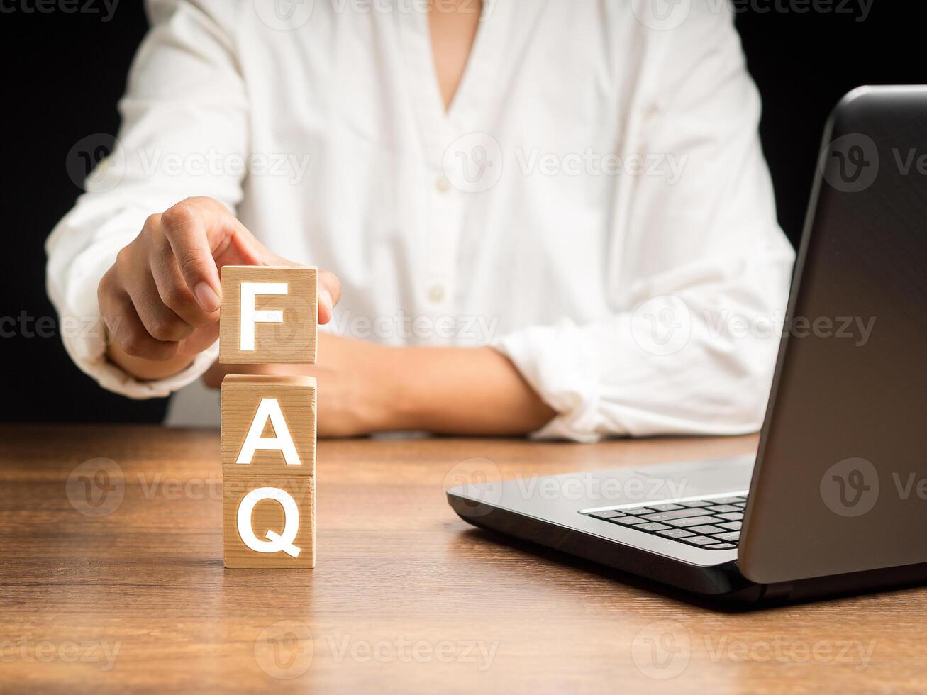Hand holding a wooden cube with letters FAQ on a wooden desk in the office photo