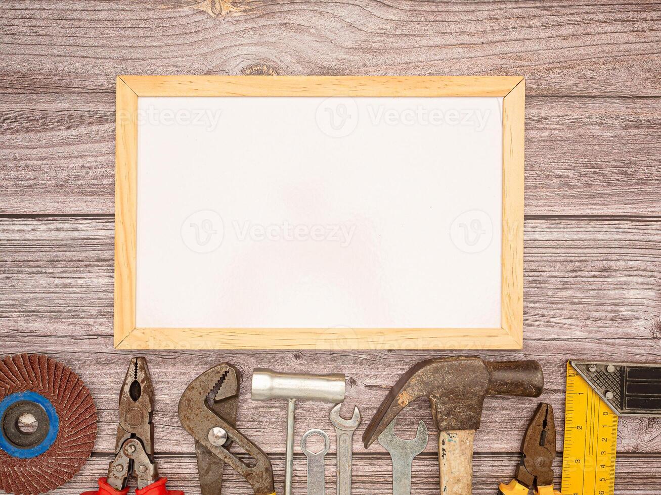 A white mini-board, construction tools, a hammer, screwdriver, screws, and pliers on a wooden table photo
