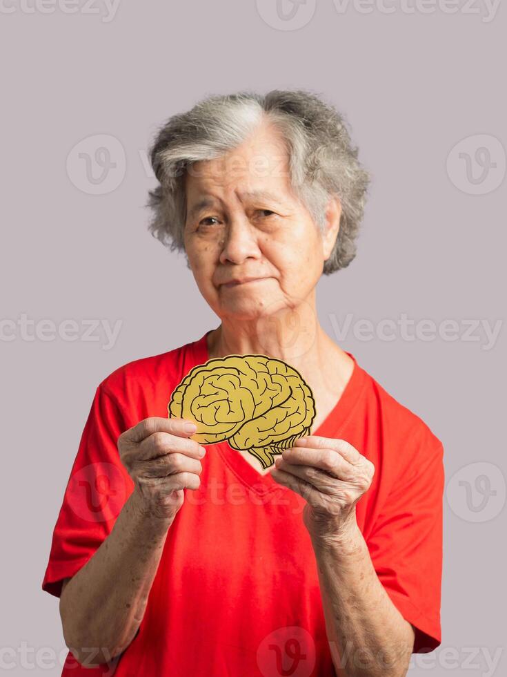 Portrait of a senior woman holding a brain symbol while standing on a gray background photo