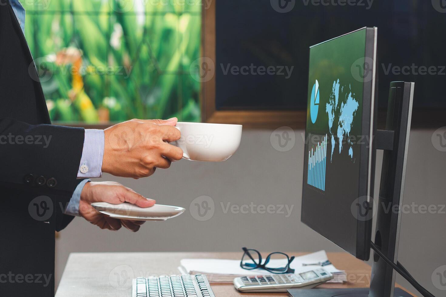 Businessman hand holding a cup of coffee and looking report on-screen monitor computer while standing at the offic photo