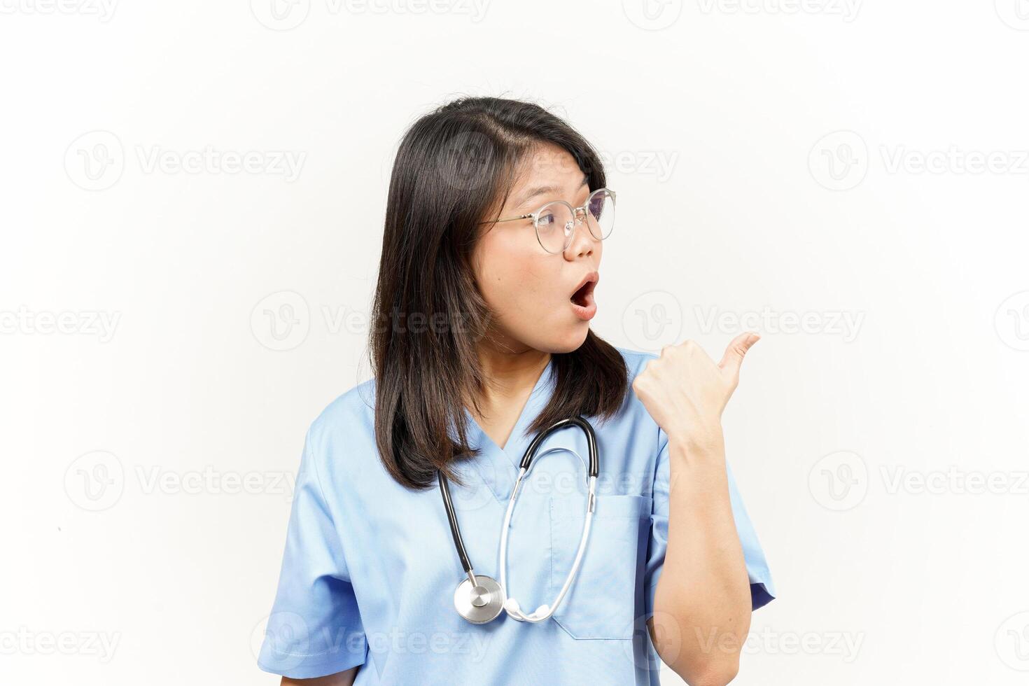 Showing and Pointing Product With Thumb Of Asian Young Doctor Isolated On White Background photo
