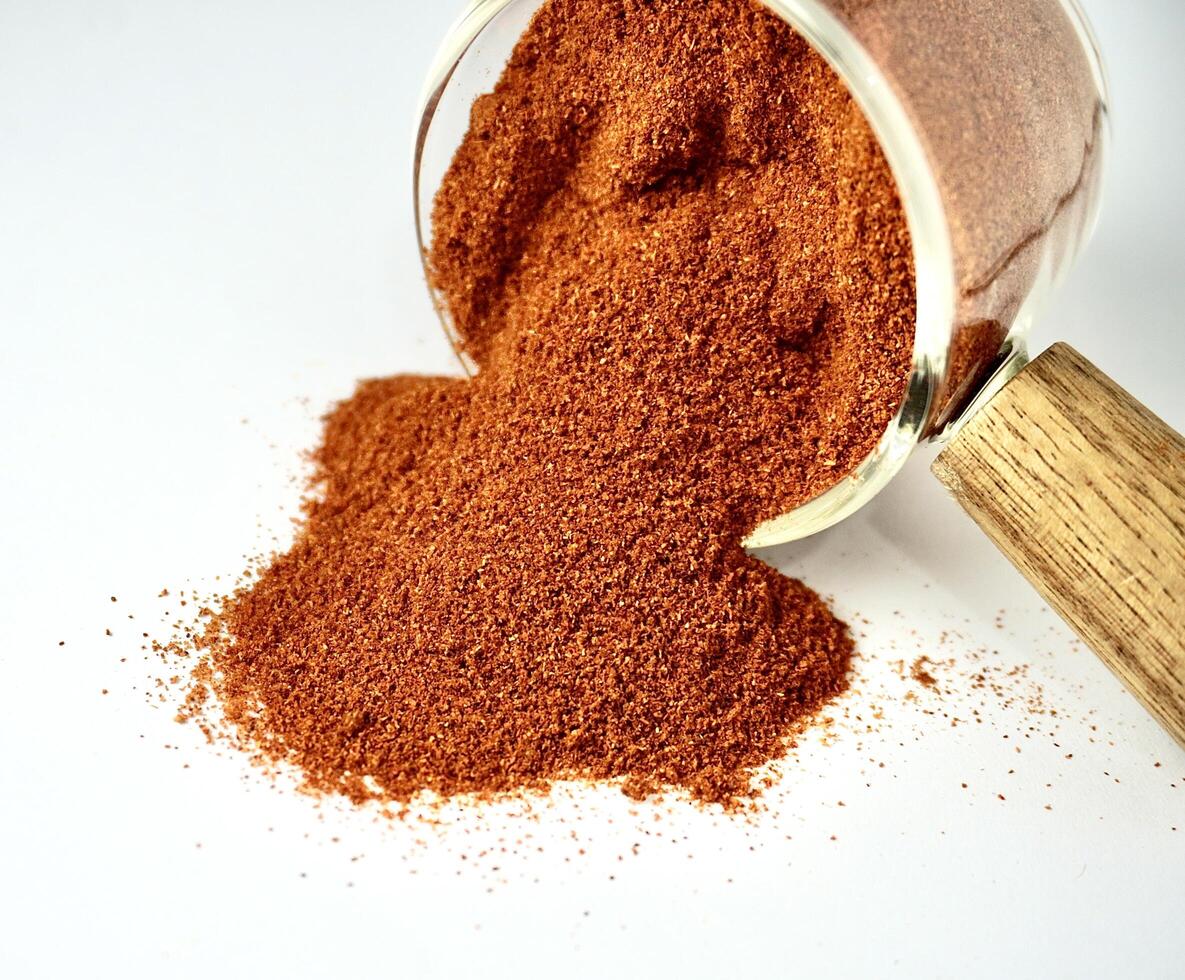 Red paprika powder food ingredients spilled from small glassware cup isolated on horizontal white background. photo