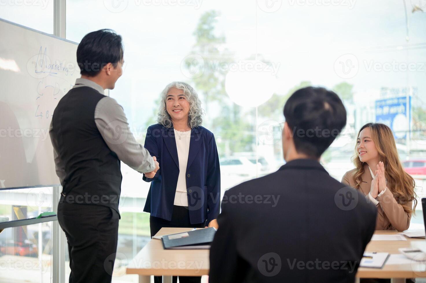 A successful senior Asian female CEO shaking hands with a young, smart male CEO during a meeting. photo