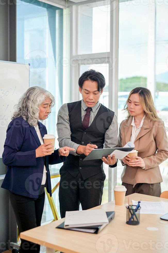 Diverse Asian businesspeople stand together in a modern office, focused on discussing work. photo
