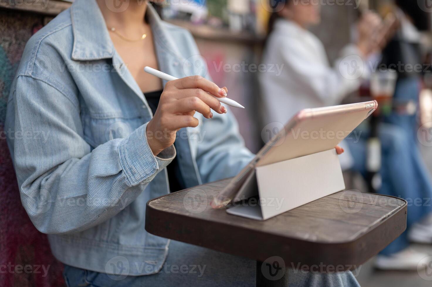 A close-up of a woman sits at an outdoor table of a cafe in the city, using her digital tablet. photo