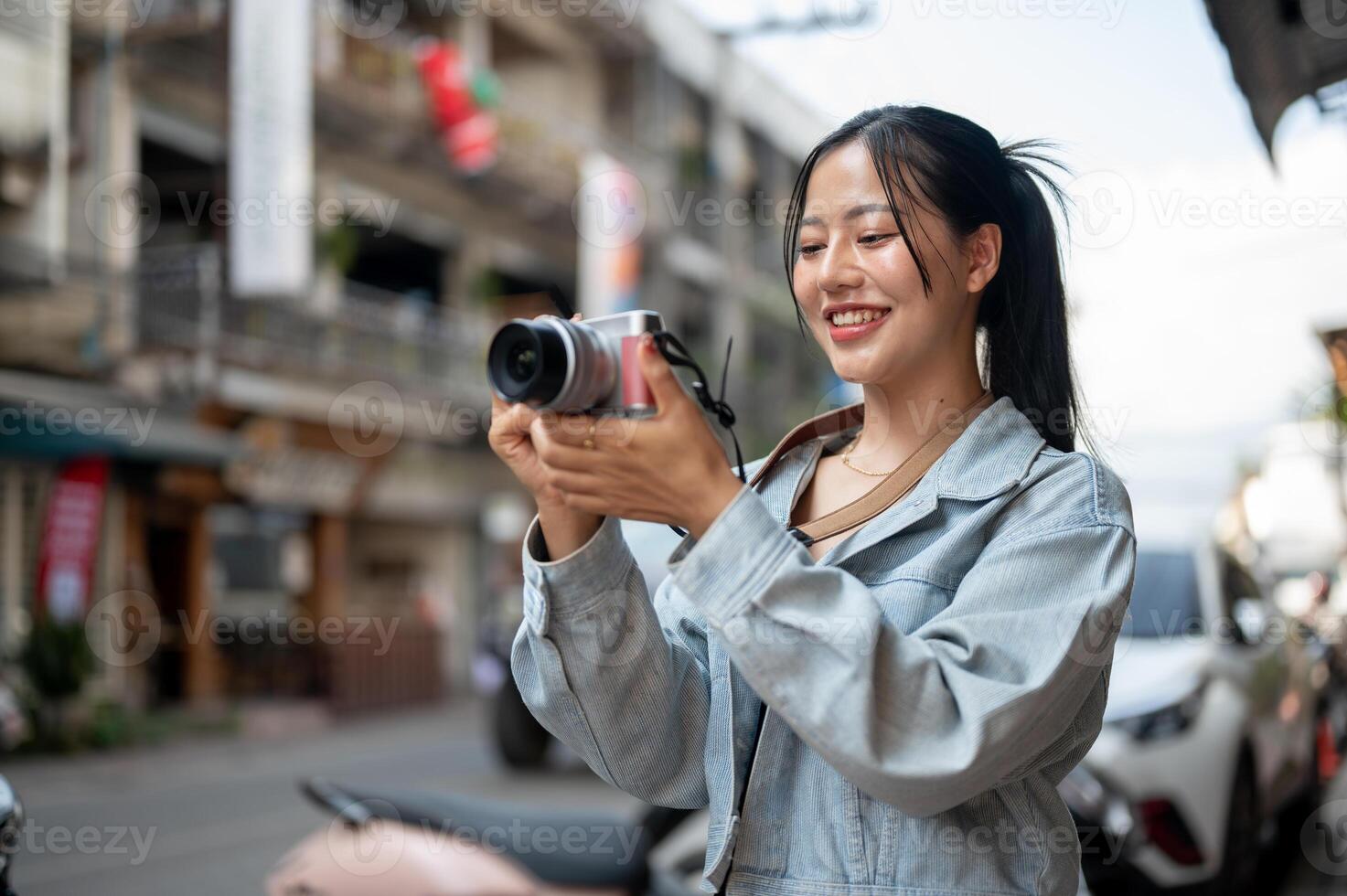 A happy Asian female tourist enjoying taking photos with her camera while exploring the city.