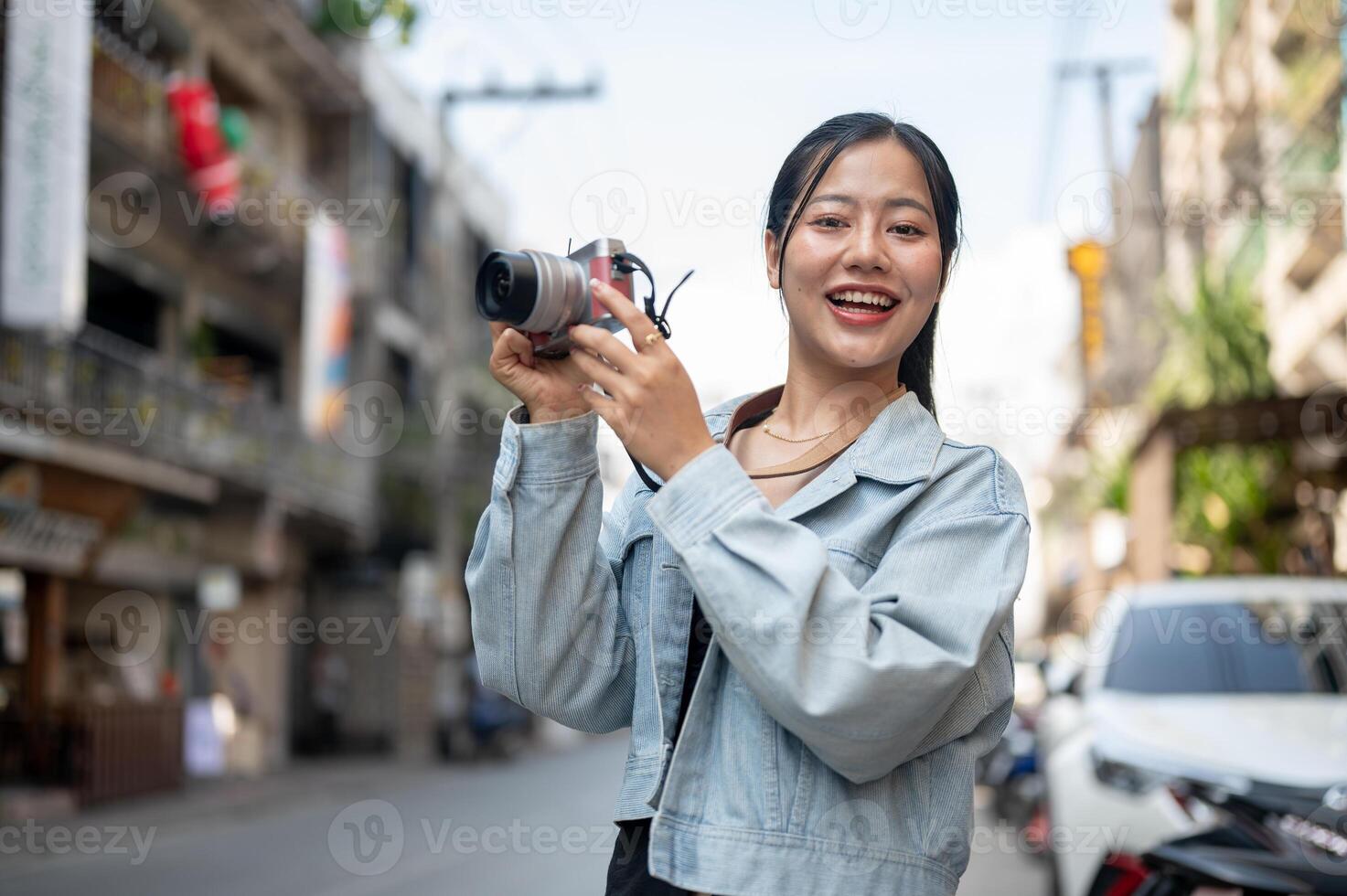 A happy Asian female tourist enjoying taking photos while exploring the city, smiling at the camera.