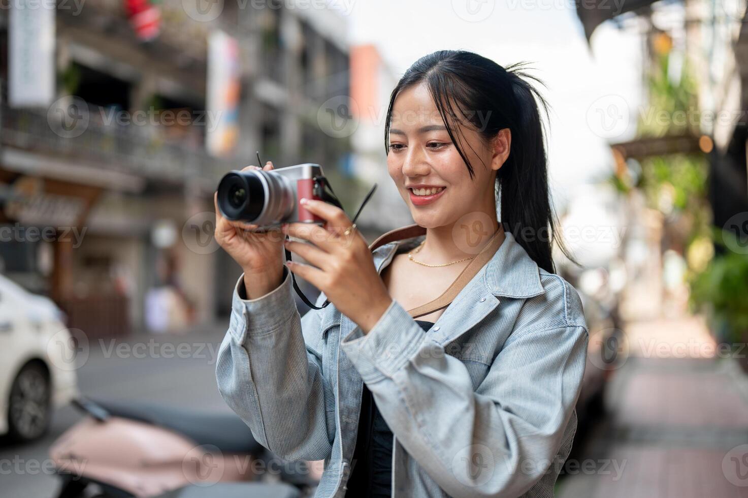 A happy Asian female tourist enjoying taking photos with her camera while exploring the city.