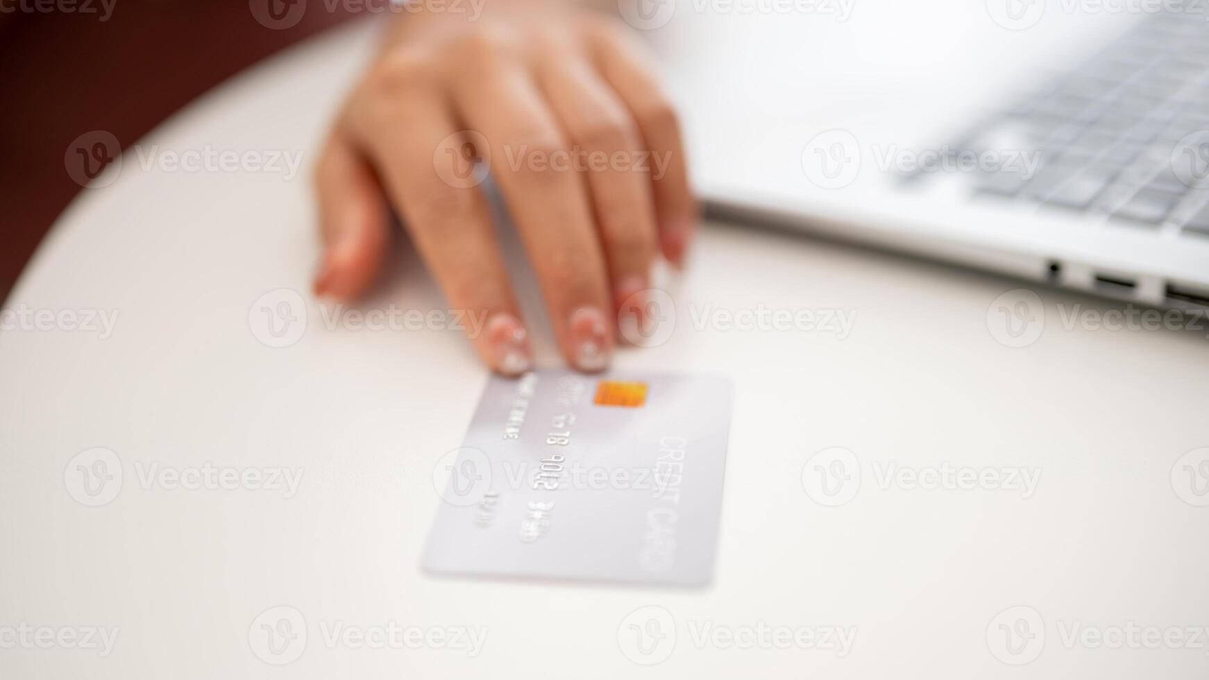 A close-up of an Asian woman showing her credit card to the camera while sitting indoors. photo