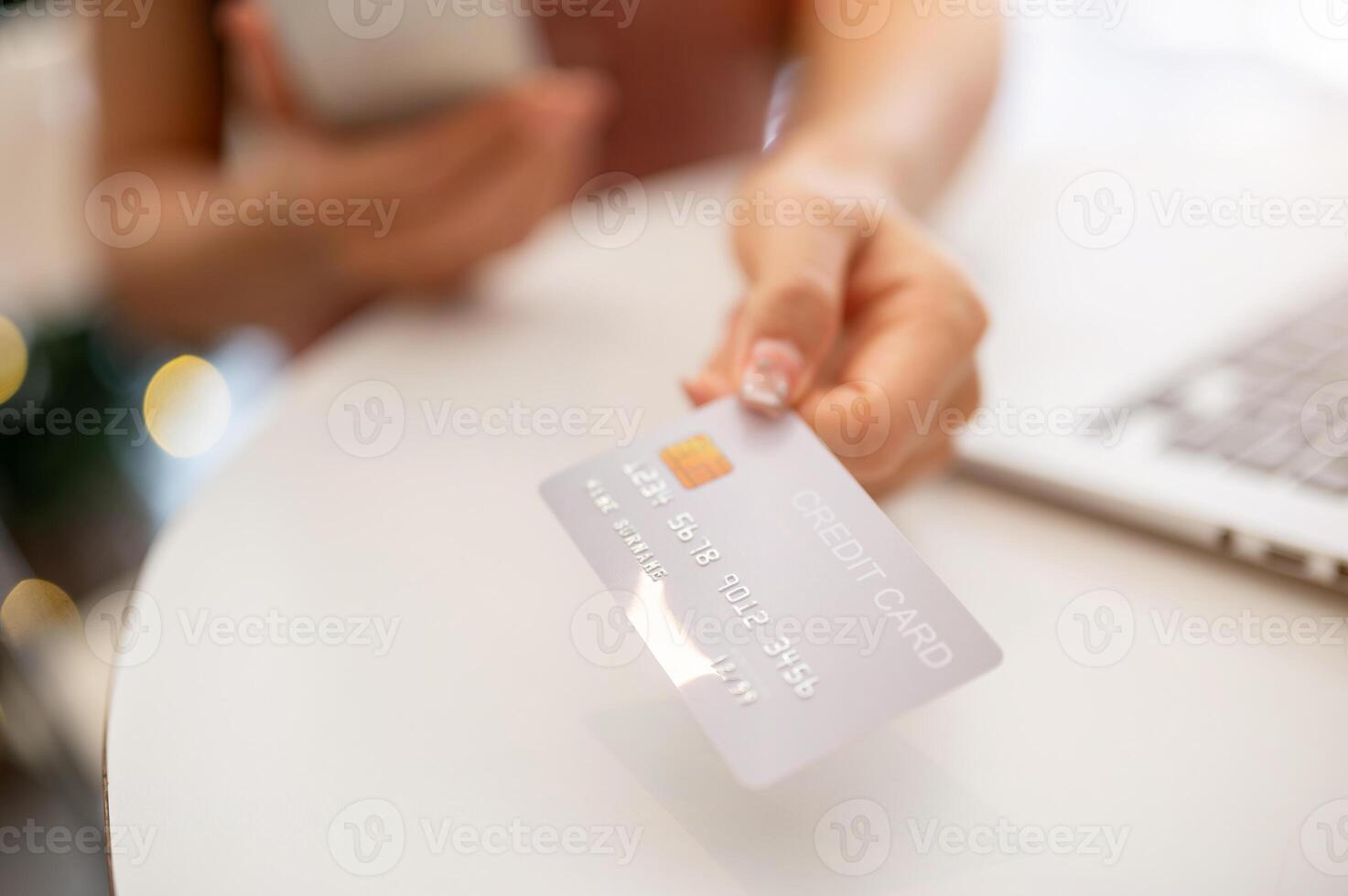 A close-up of an Asian woman showing her credit card to the camera while sitting indoors. photo