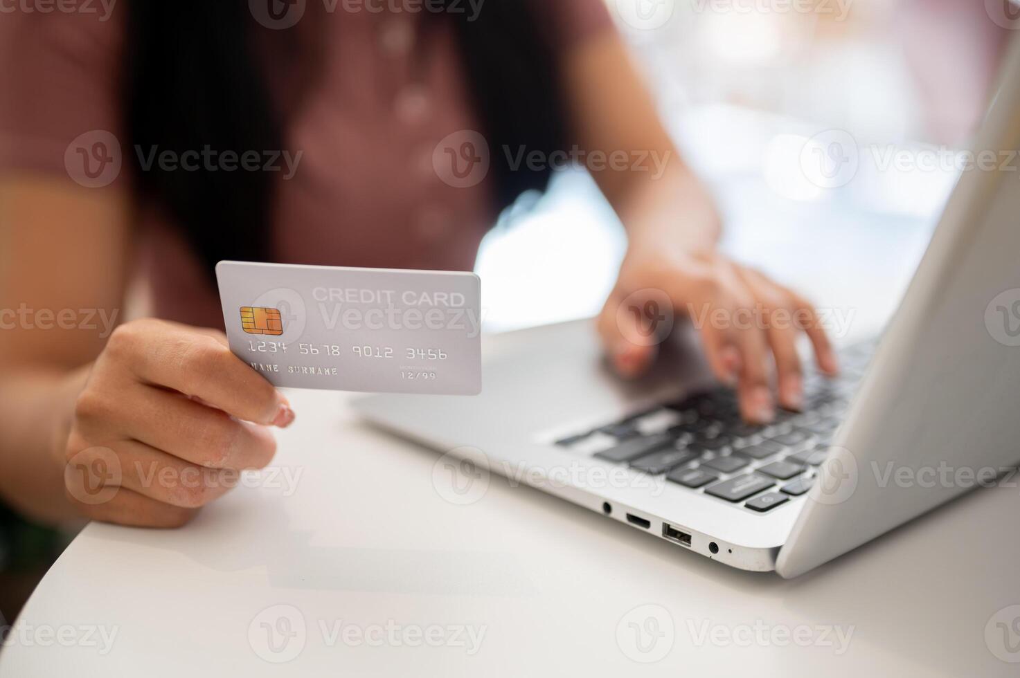 A close-up of a woman showing her credit card to the camera while using her laptop. photo