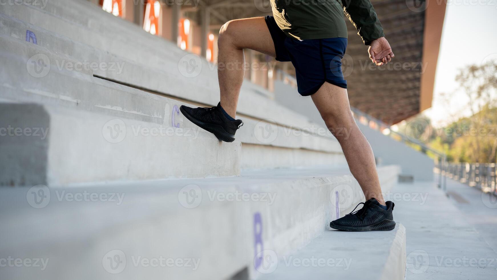 A cropped image of a man in sportswear running up the steps of a stadium, exercising in the morning. photo