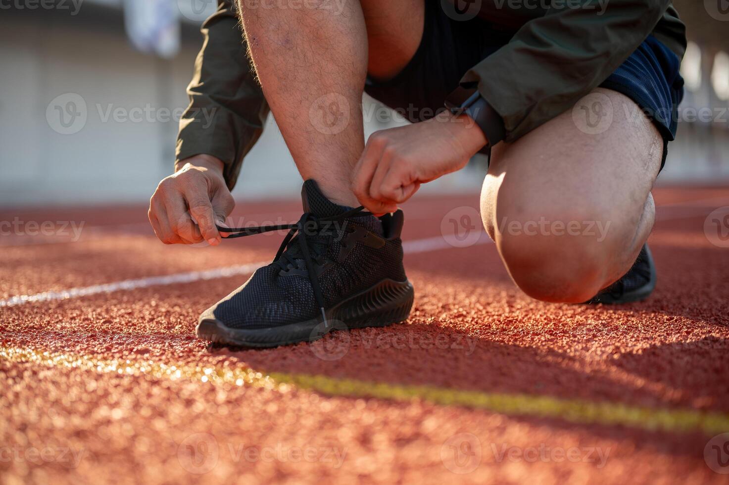 A close-up of an athletic male runner tying his running shoes, getting ready to run at a stadium. photo