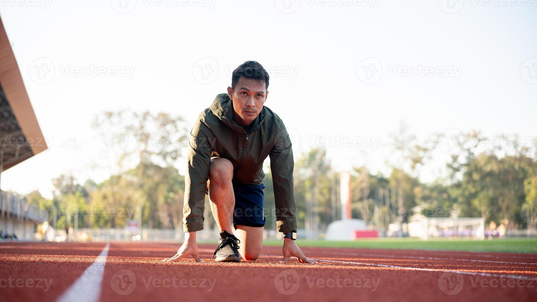 An Asian athletic male runner in sportswear trains at a stadium, getting ready at the starting line. photo