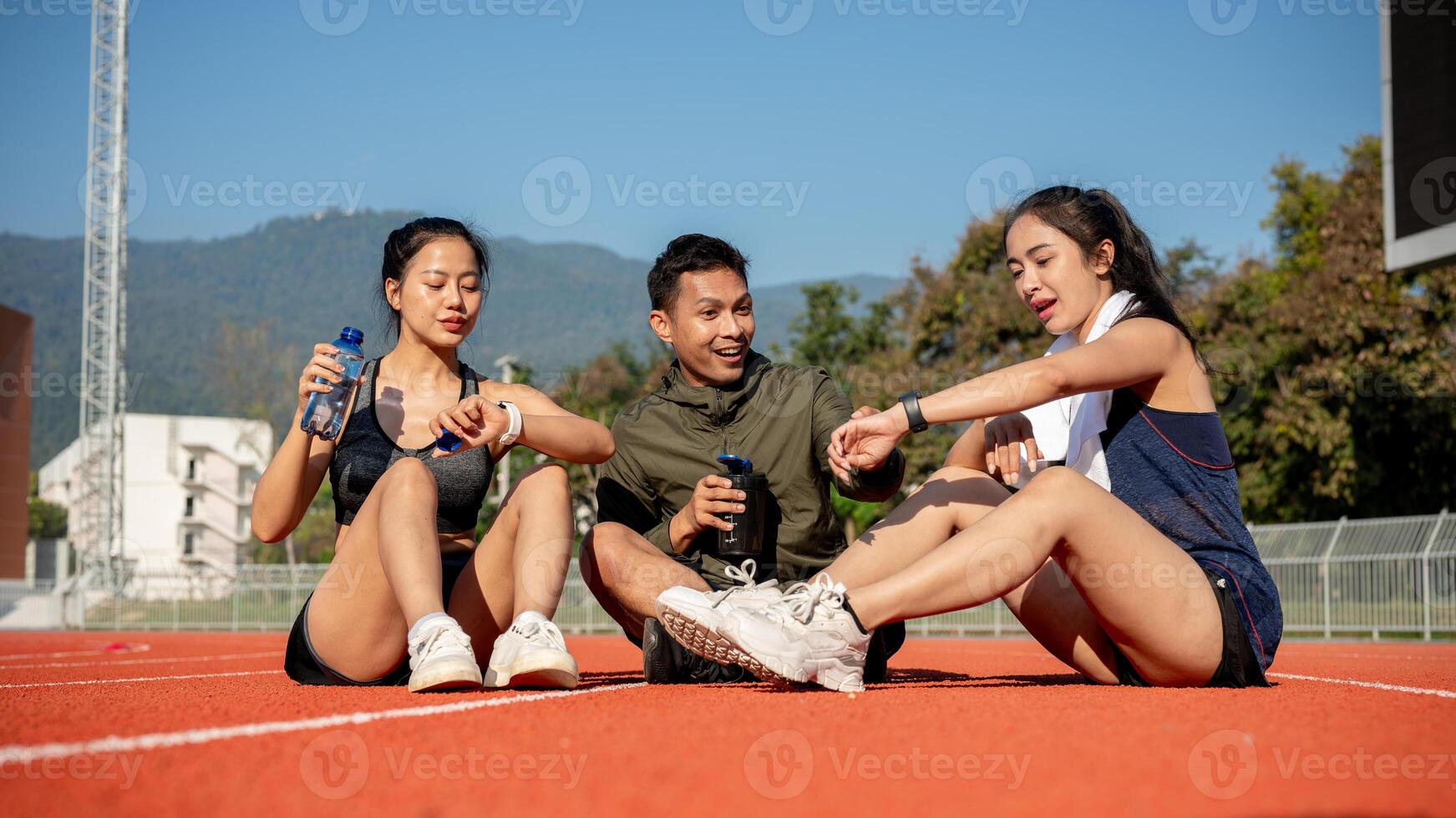 Portrait of a group of cheerful Asian athlete friends resting on a sports track after training. photo