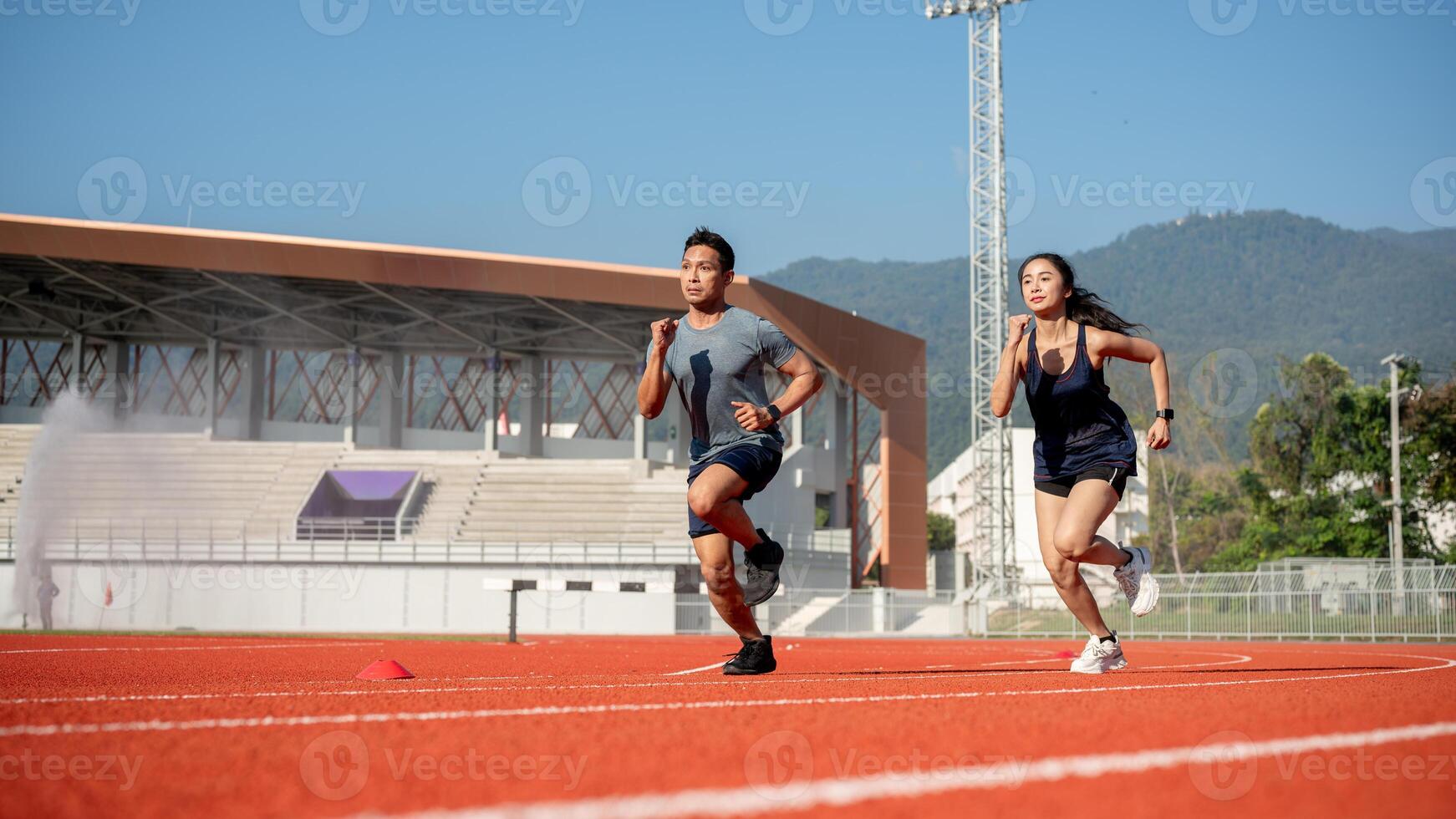 Two determined Asian athletes running on a track in a stadium on a sunny day. photo