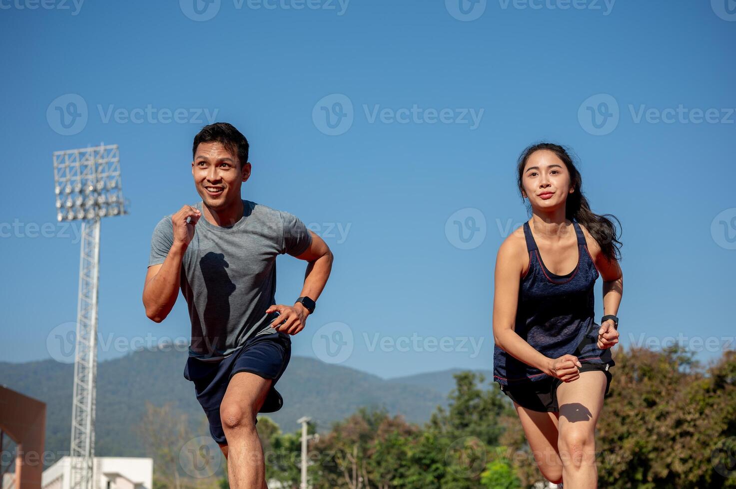 Two determined Asian athletes running on a track in a stadium on a sunny day. photo