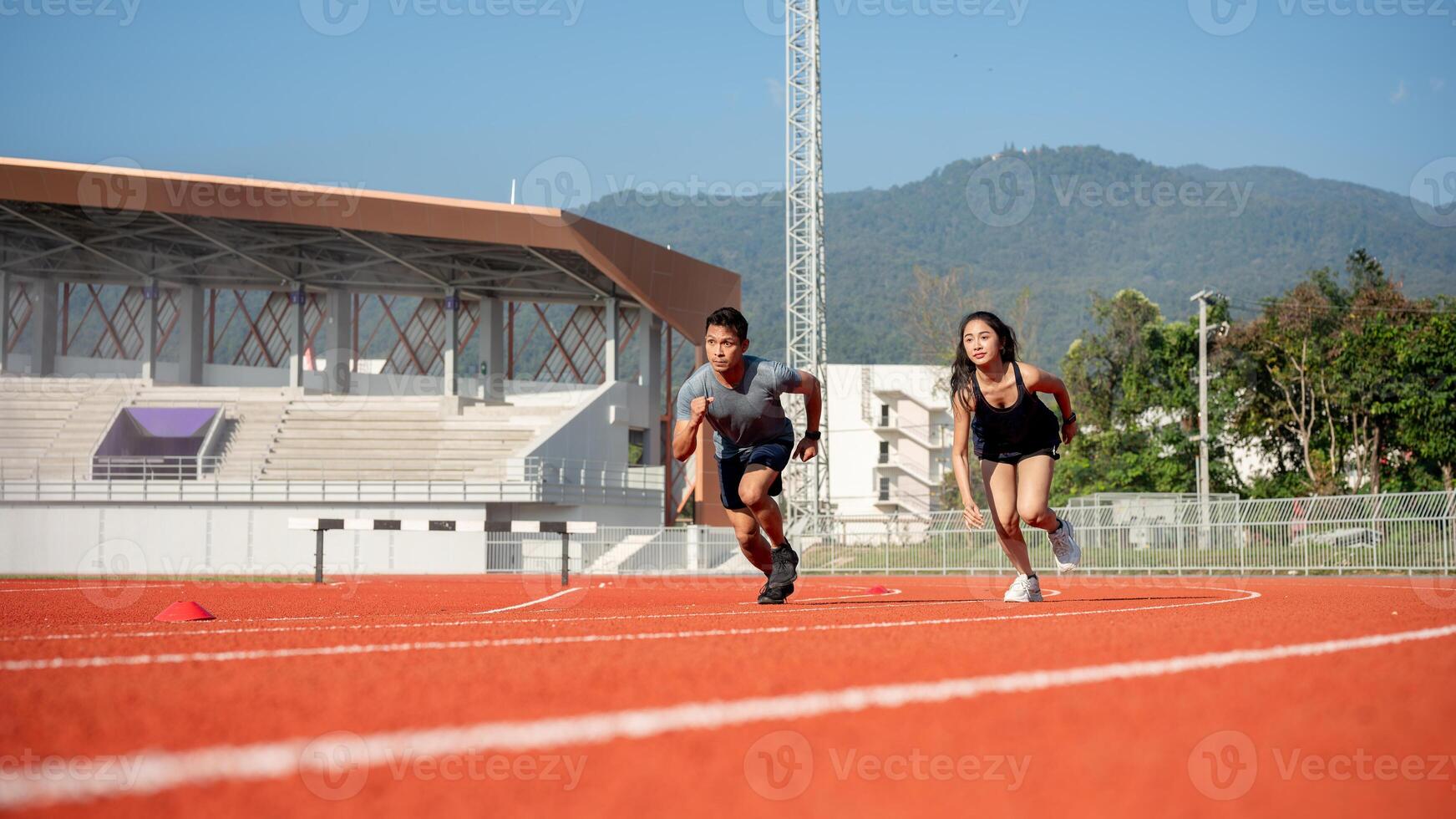 Two determined Asian athletes running on a track in a stadium on a sunny day. photo