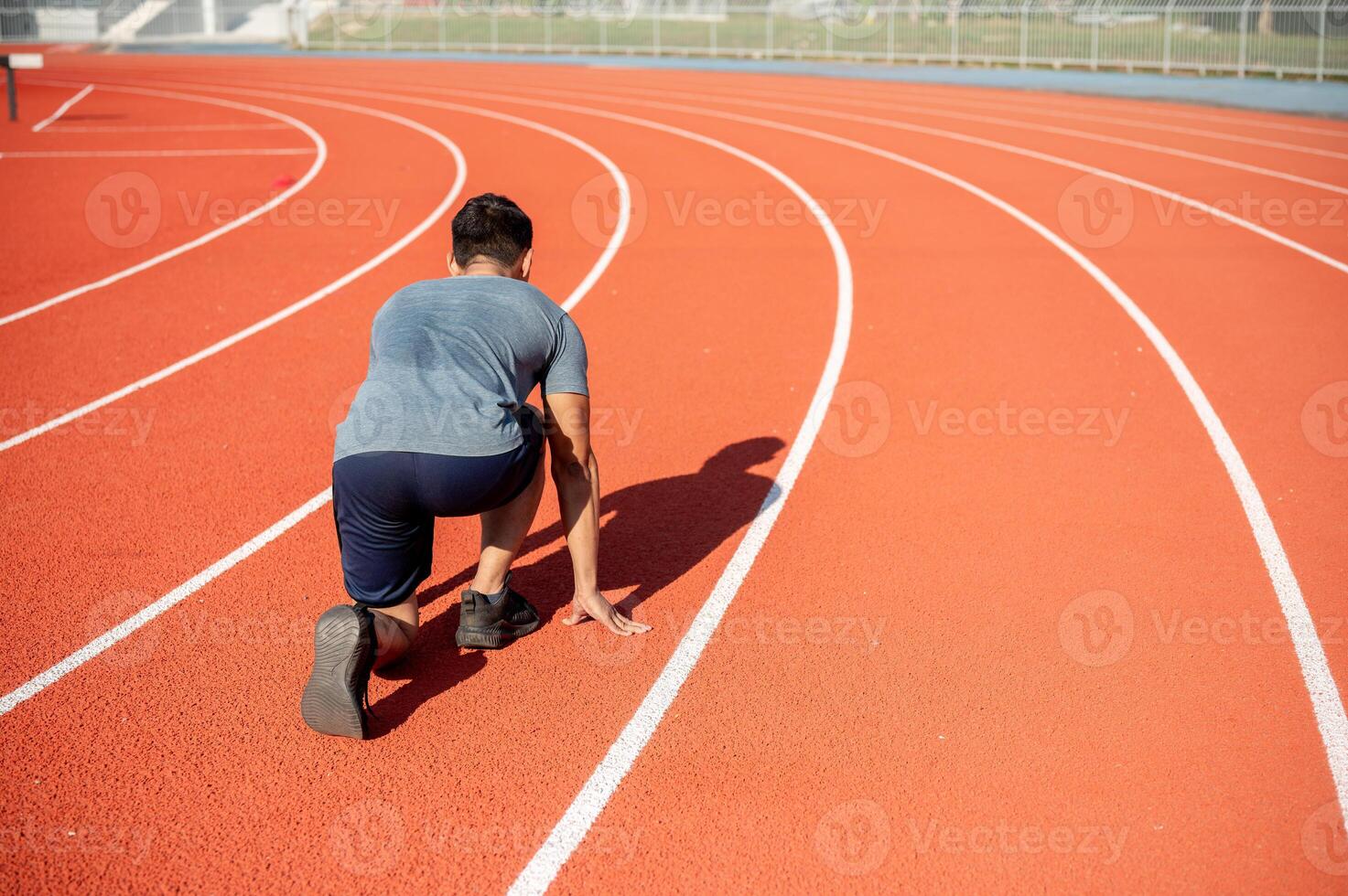 A strong Asian athletic male runner in sportswear trains at a stadium, preparing to run photo