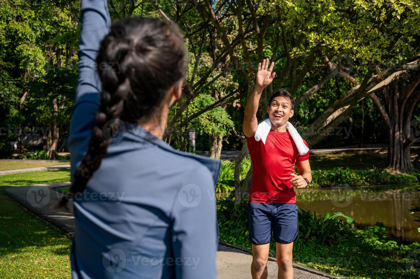 Cheerful Asian man waves and greets his friend as they bump into each other while jogging in a park. photo