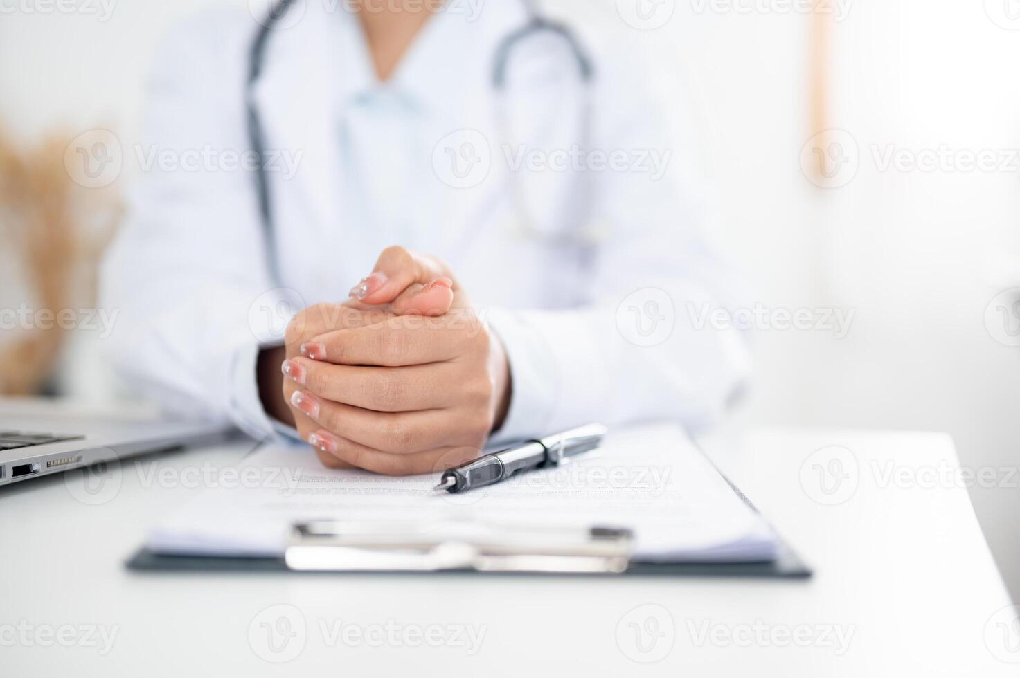 A doctor sitting at her desk with her hands clasped together, displaying a serious expression. photo