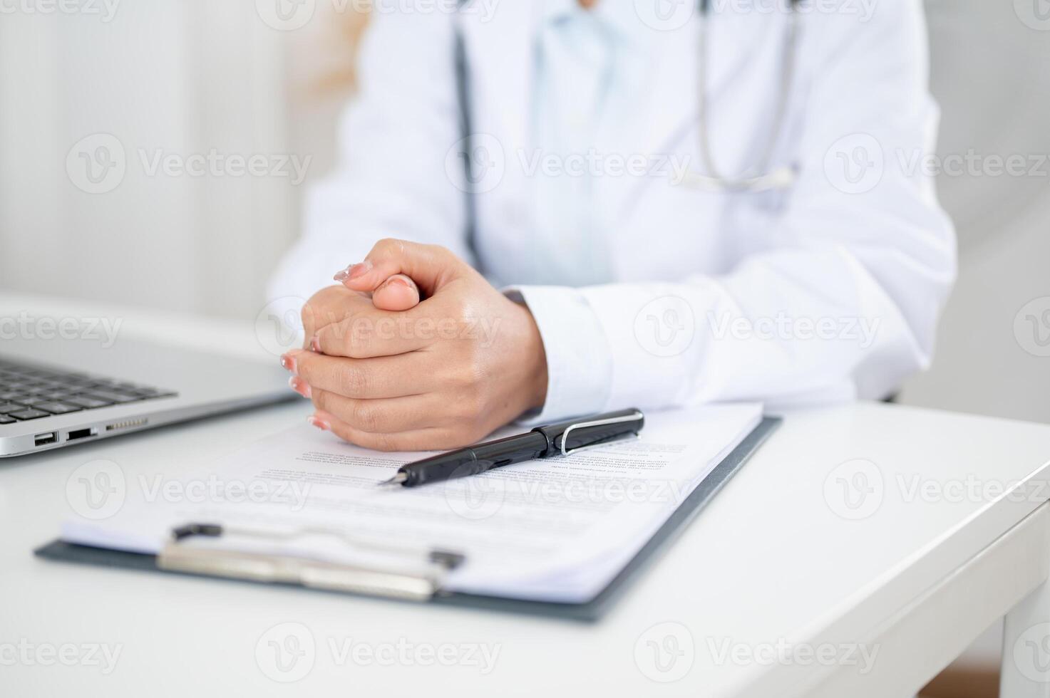 A doctor sitting at her desk with her hands clasped together, displaying a serious expression. photo