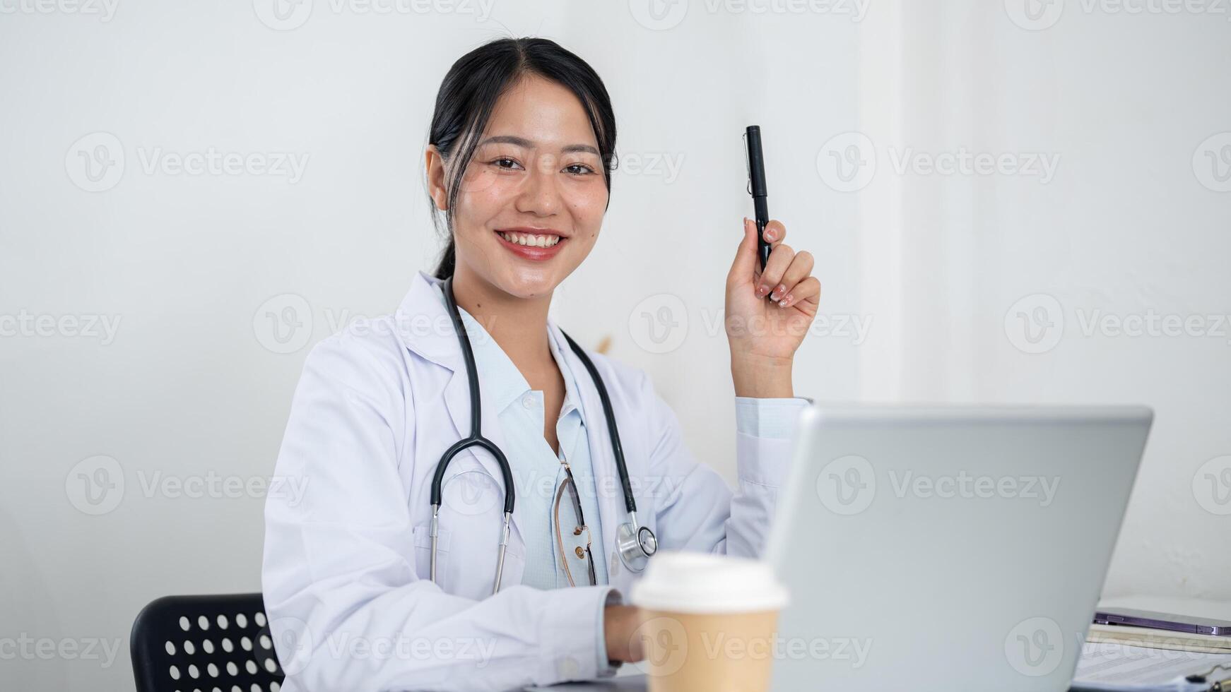 A confident female doctor sits at her desk, holding a pen upward as if she has just gotten an idea. photo
