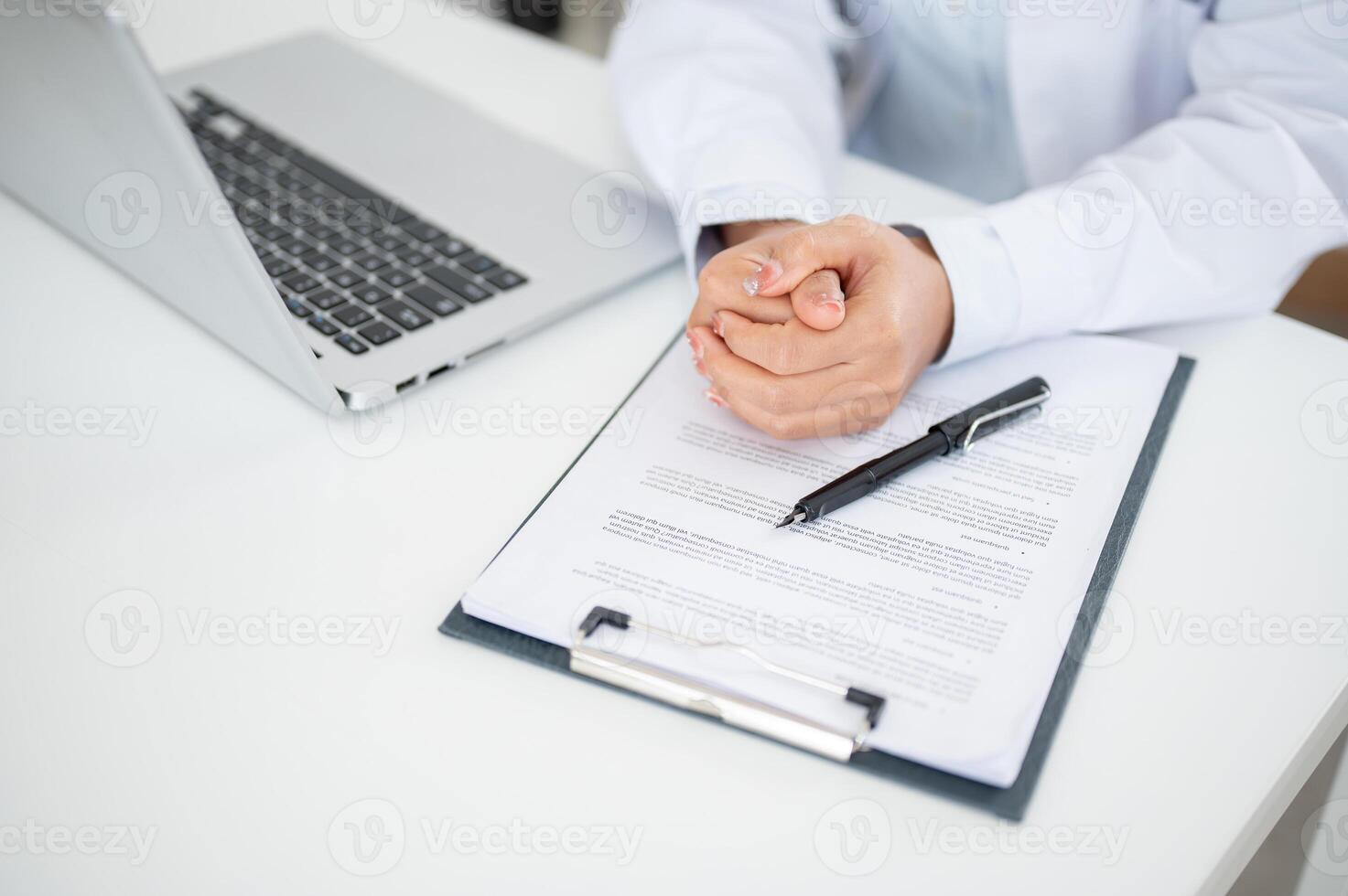 A doctor sitting at her desk with her hands clasped together, displaying a serious expression. photo
