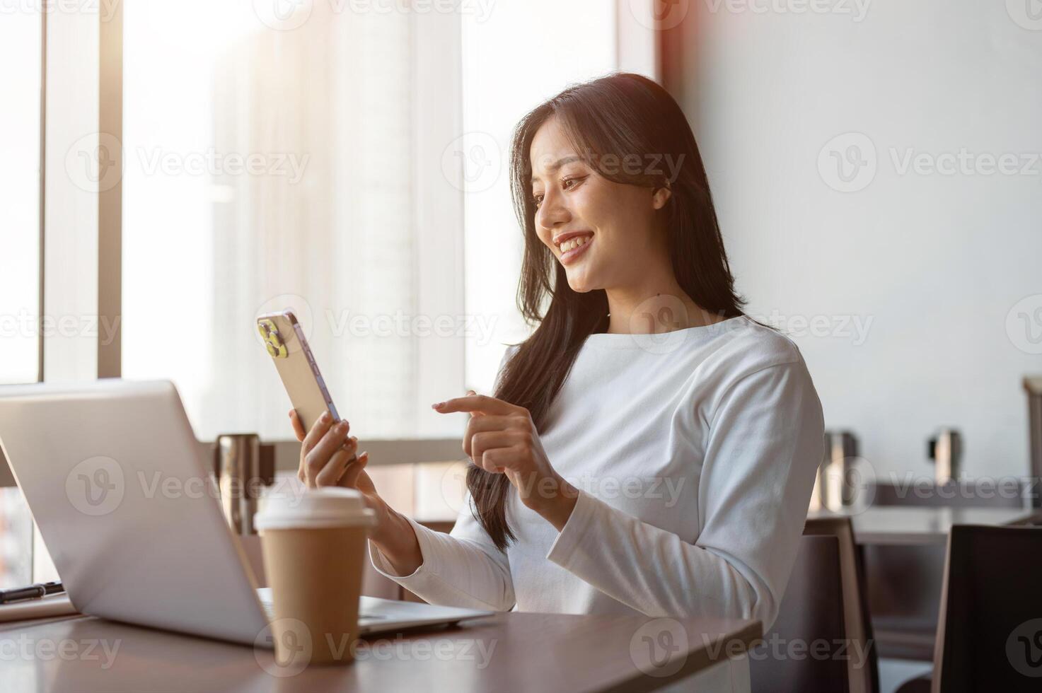 Attractive Asian woman reading messages on her smartphone while working remotely from a coffee shop. photo
